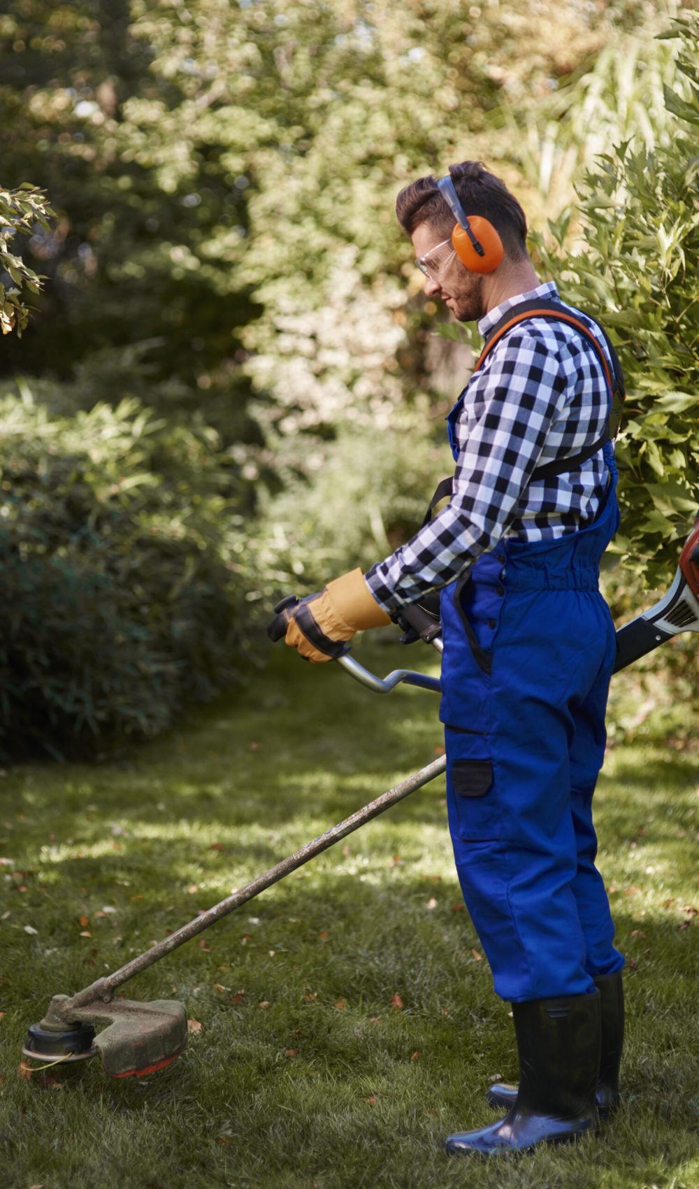 Busy man using a weedwacker at garden